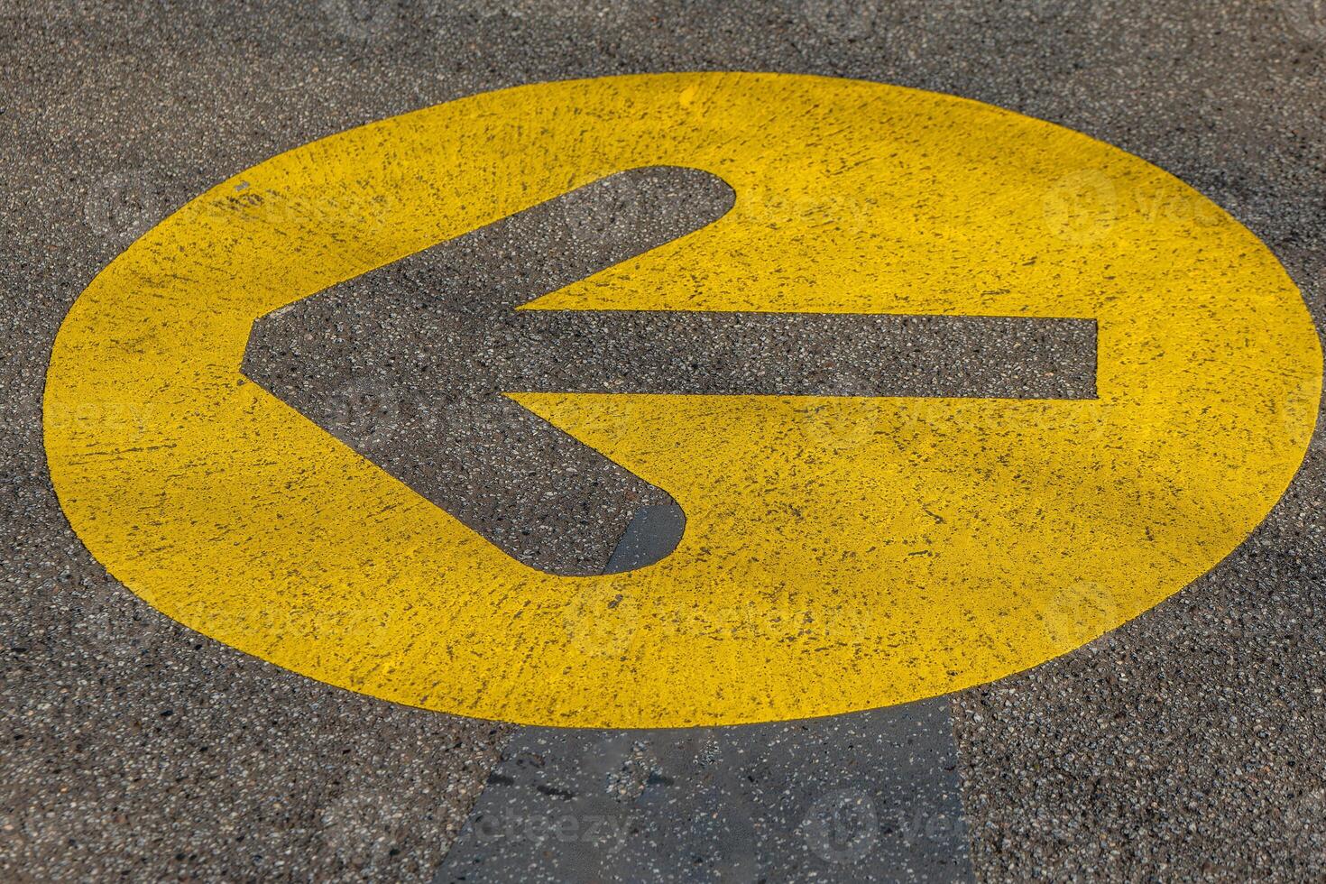 black arrow with a yellow circle pointing to the left is painted on a road photo