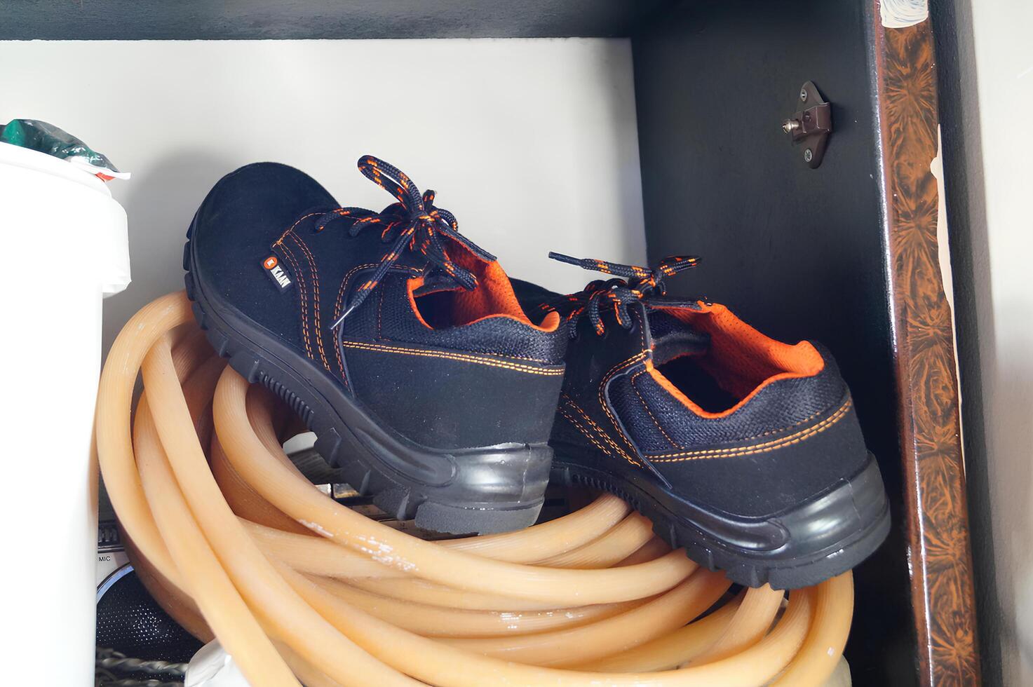 un par de botas descansando en enroscado naranja manguera dentro un gabinete foto