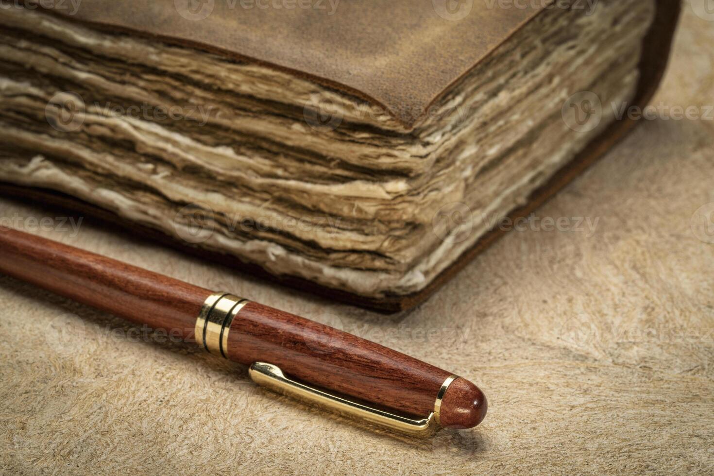 stylish wooden pen and a retro leather-bound journal with decked edge handmade paper pages on a textured bark paper, journaling concept photo