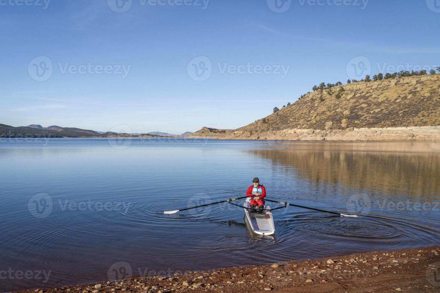 Senior male rower is rowing a coastal rowing shell - Carter Lake in fall or winter scenery in northern Colorado. photo