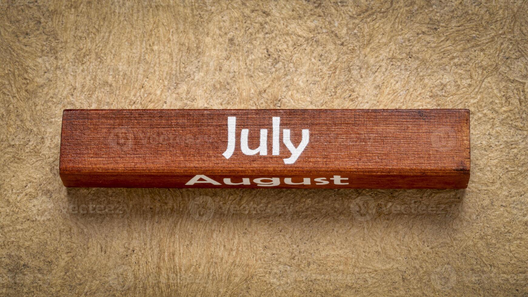 July and August text on wooden block against handmade bark paper in earth tones, calendar concept photo