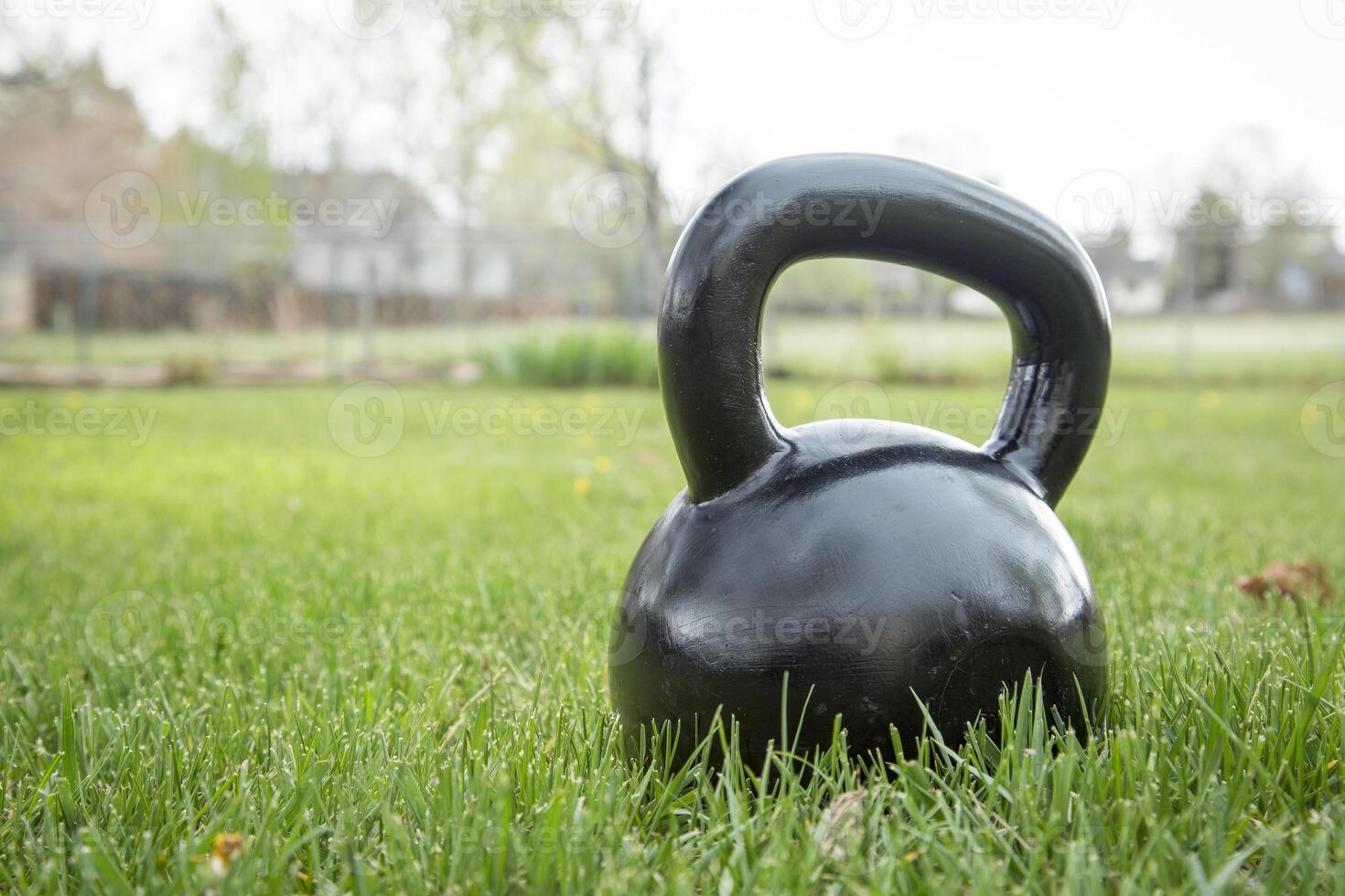 heavy iron black kettlebell on green grass in backyard - outdoor fitness concept photo