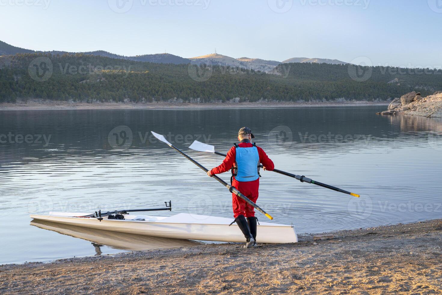 Senior male rower with a coastal rowing shell and hatchet oars on a shore of Carter Lake in fall or winter scenery in northern Colorado. photo