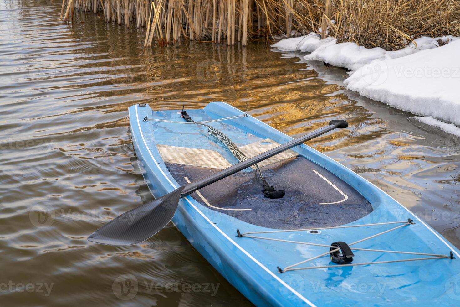 touring stand up paddleboard with a paddle and safety leash on a shore of lake in northern Colorado, winter or early spring scenery with some snow photo