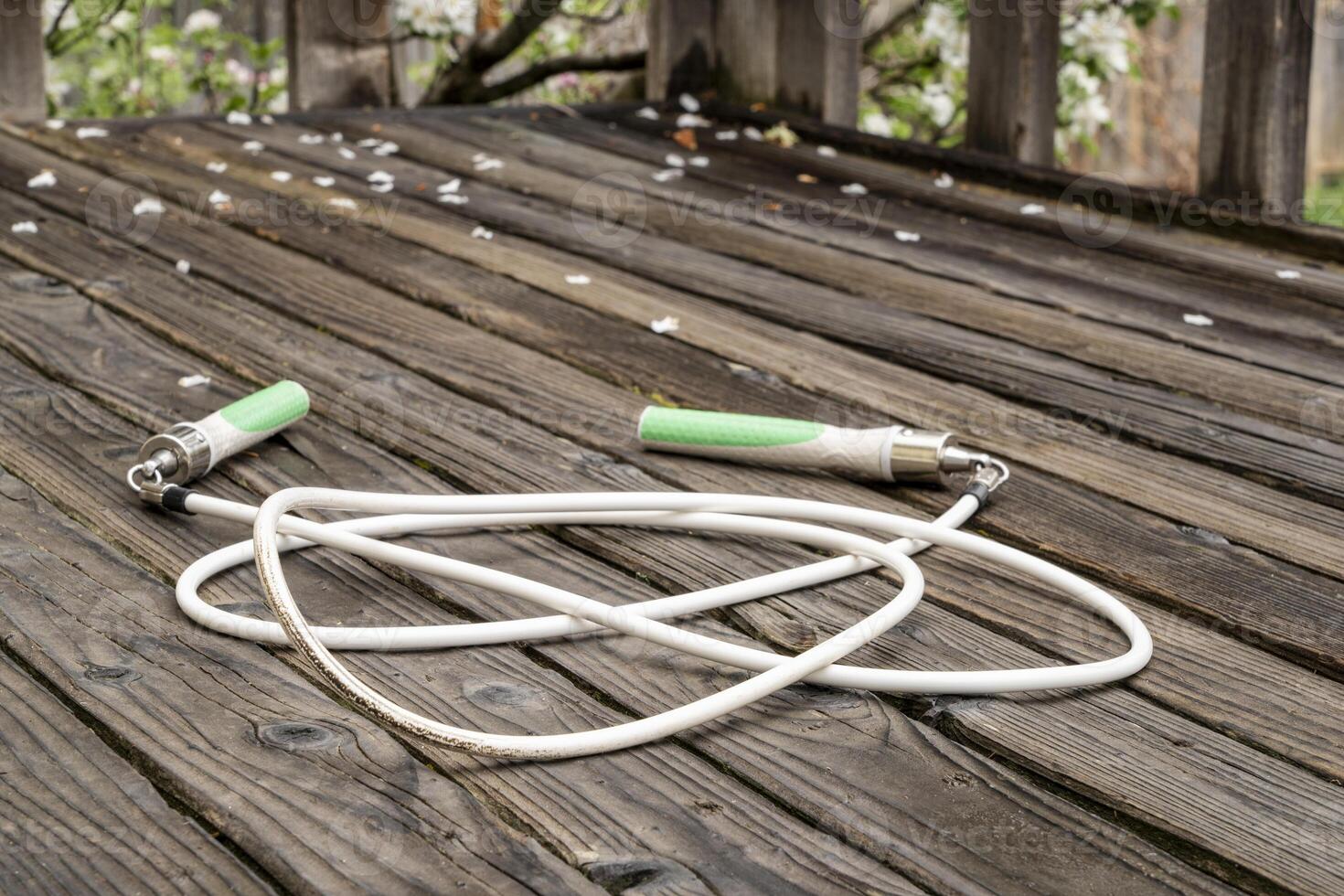 heavy fitness jump rope on a rustic, weathered wooden backyard deck in springtime scenery photo