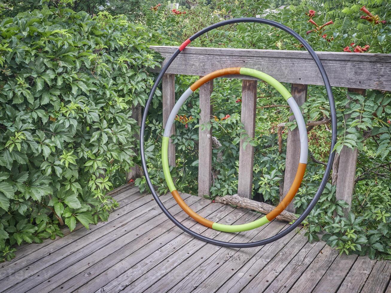 weighted hula hoop and one home made from a sprinkler pipe on a wooden backyard deck in summer scenery, core workout concept photo