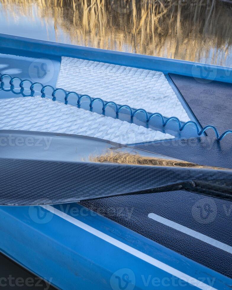 wet paddle and a coiled safety leash on a deck of stand up paddleboard photo