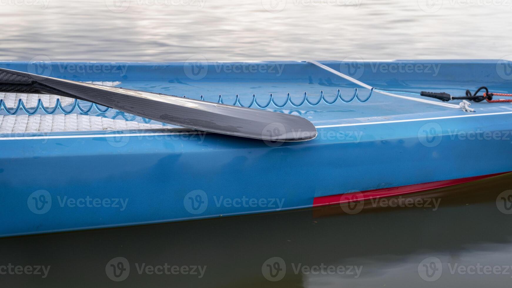 wet paddle and a coiled safety leash on a deck of stand up paddleboard photo