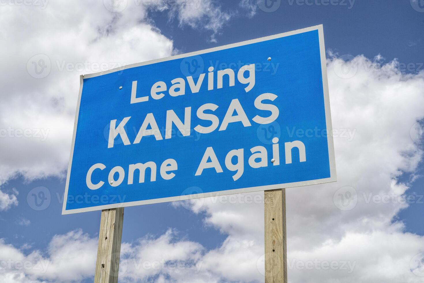 Leaving Kansas, come again - roadside sign at highway against cloudy sky photo