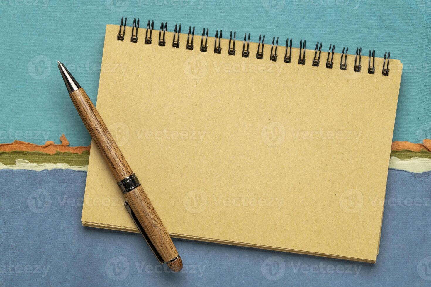 blank spiral sketchbook with a pen against colorful abstract landscape photo