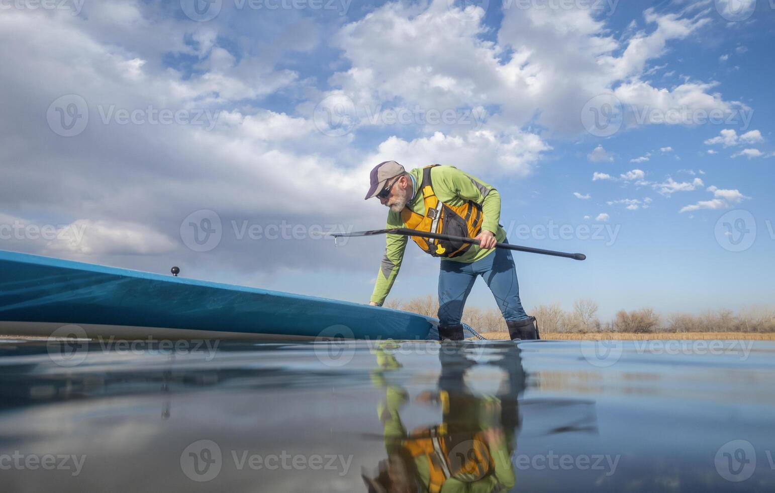 senior paddler and his paddleboard on lake in winter or early spring in Colorado, frog perspective, partially submerged action camera photo