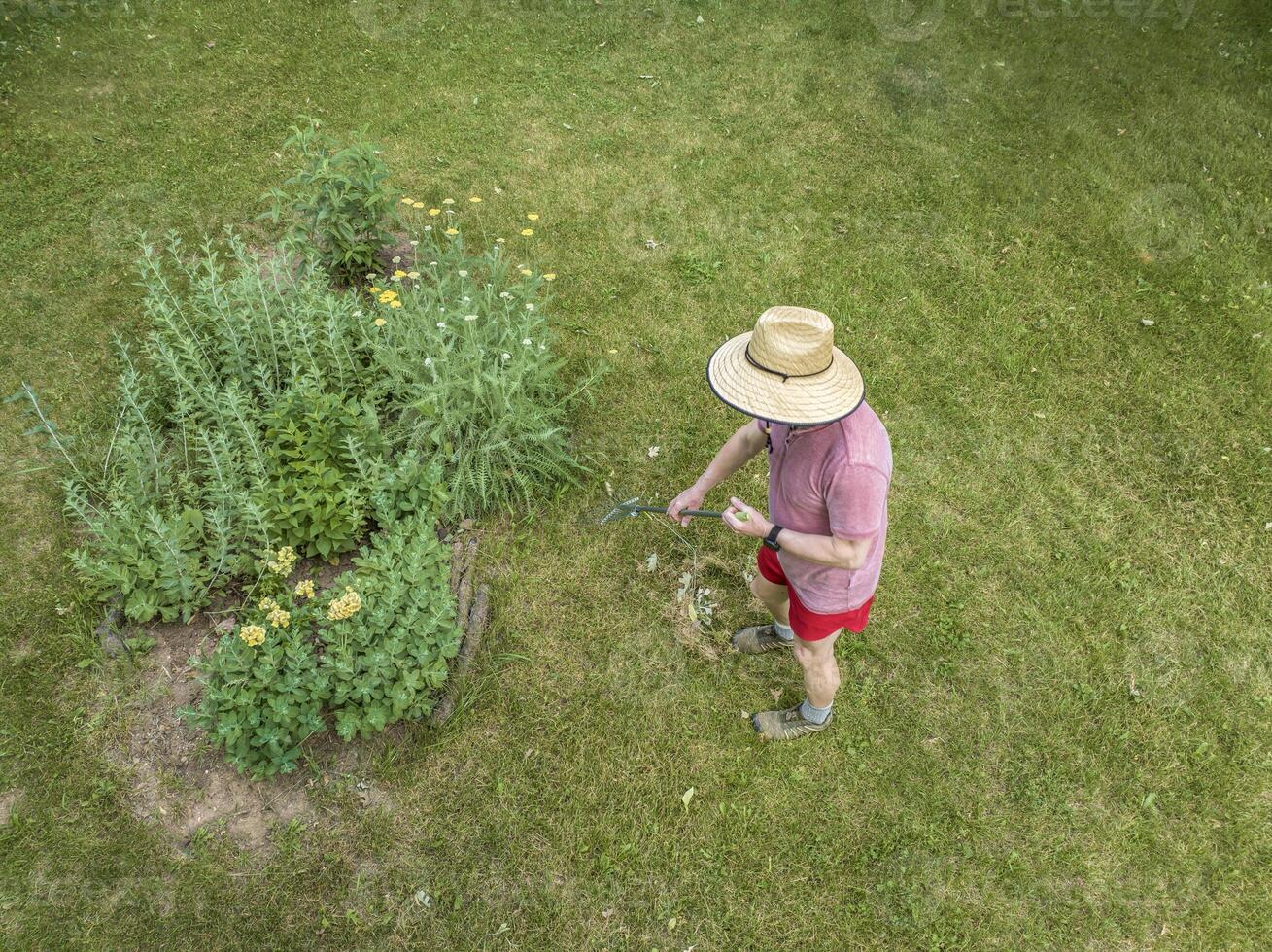 aerial view of a man in a big straw sun hat raking lawn photo