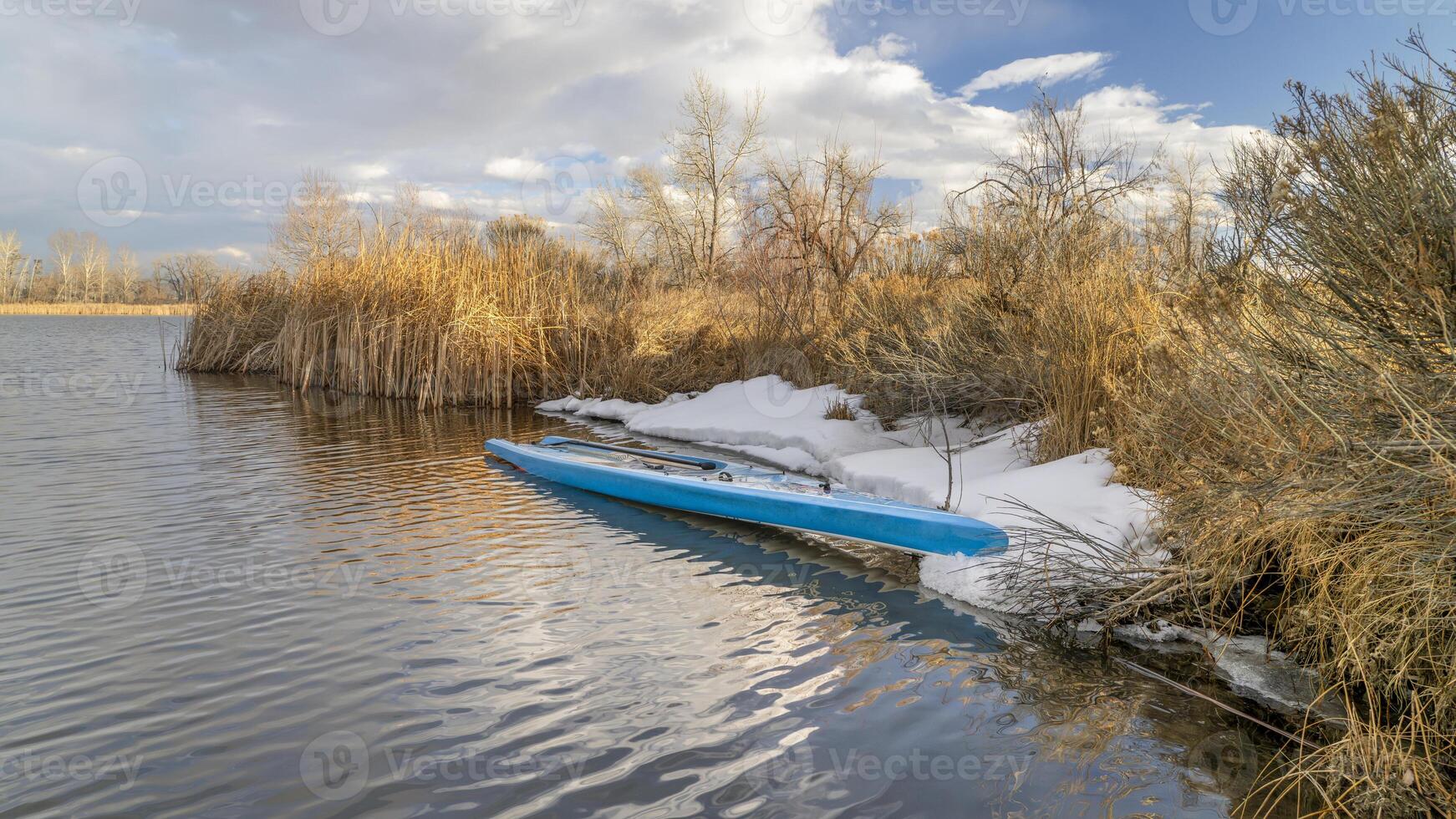 turismo estar arriba paddleboard con un paleta y la seguridad Correa en un apuntalar de lago en del Norte Colorado, invierno o temprano primavera paisaje con algunos nieve foto