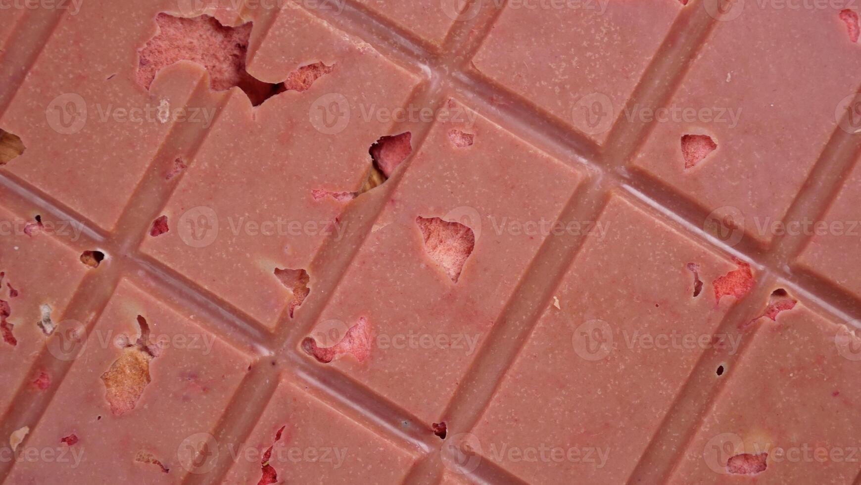 A bar of pink ruby chocolate with freeze-dried strawberries and almonds close-up. A healthy dessert based on berries and nuts photo