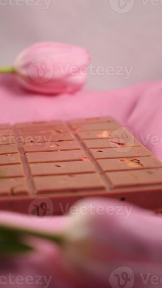 A bar of pink ruby chocolate with sublimated freeze-dried strawberries and almonds and spring tulip flowers . A dessert based on berries and nuts for International Women's Day, March 8, mother's day photo