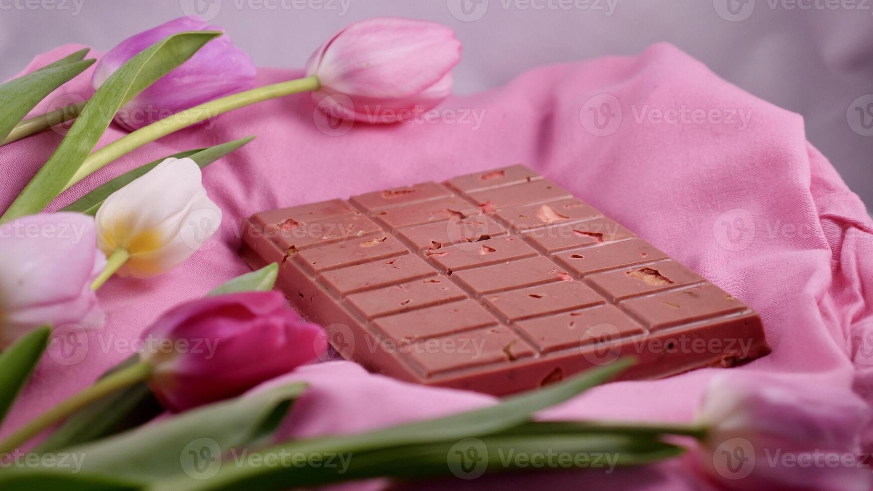 A bar of pink ruby chocolate with sublimated freeze-dried strawberries and almonds and spring tulip flowers . A dessert based on berries and nuts for International Women's Day, March 8, mother's day photo