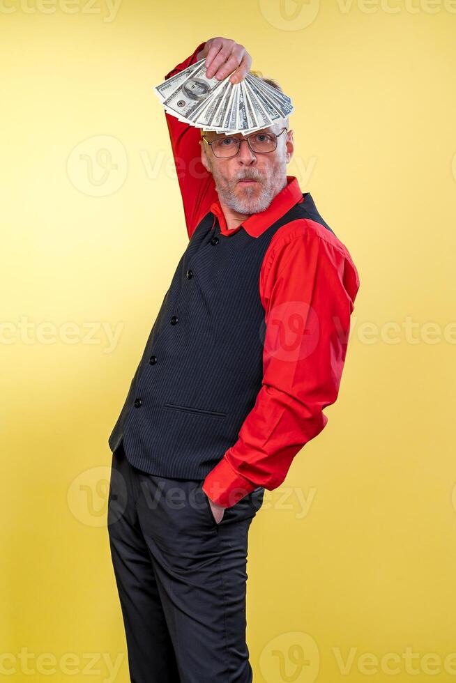 Old smiling grey-haired man in eyeglasses. Holding fan of dollars over head in dancing pose. Human emotions and facial expressions photo