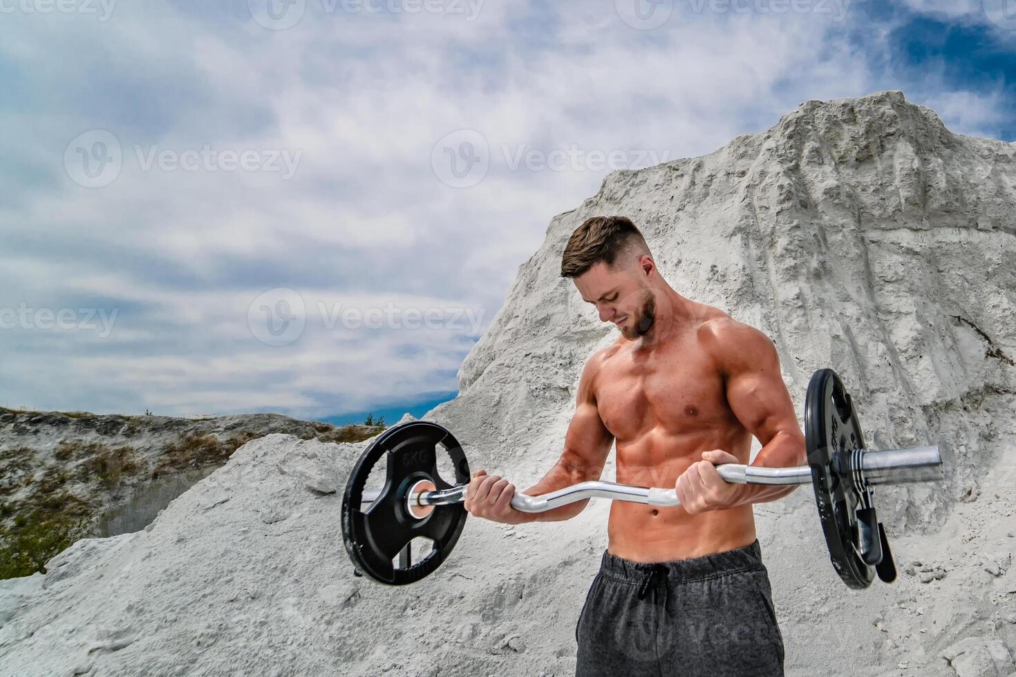 Muscular and bearded man doing exercises with barbell outdoors. Bodybuilding and outdoor sports concept. Photoshoot in a quarry. photo