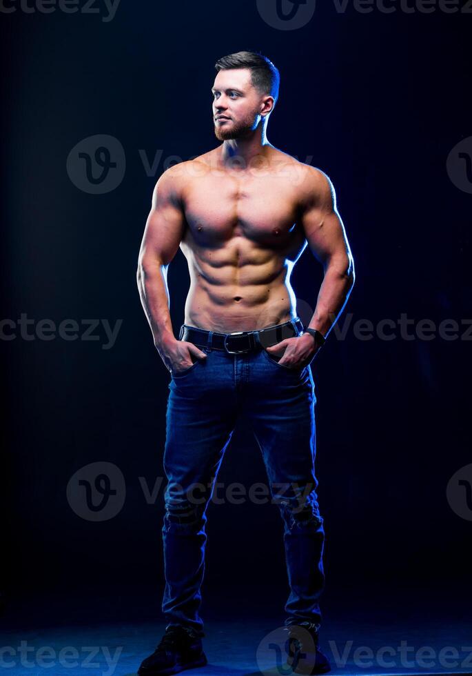 Bodybuilder posing on black background. Muscular and fit young bodybuilder fitness male model posing over dark background. Full size portrait. photo