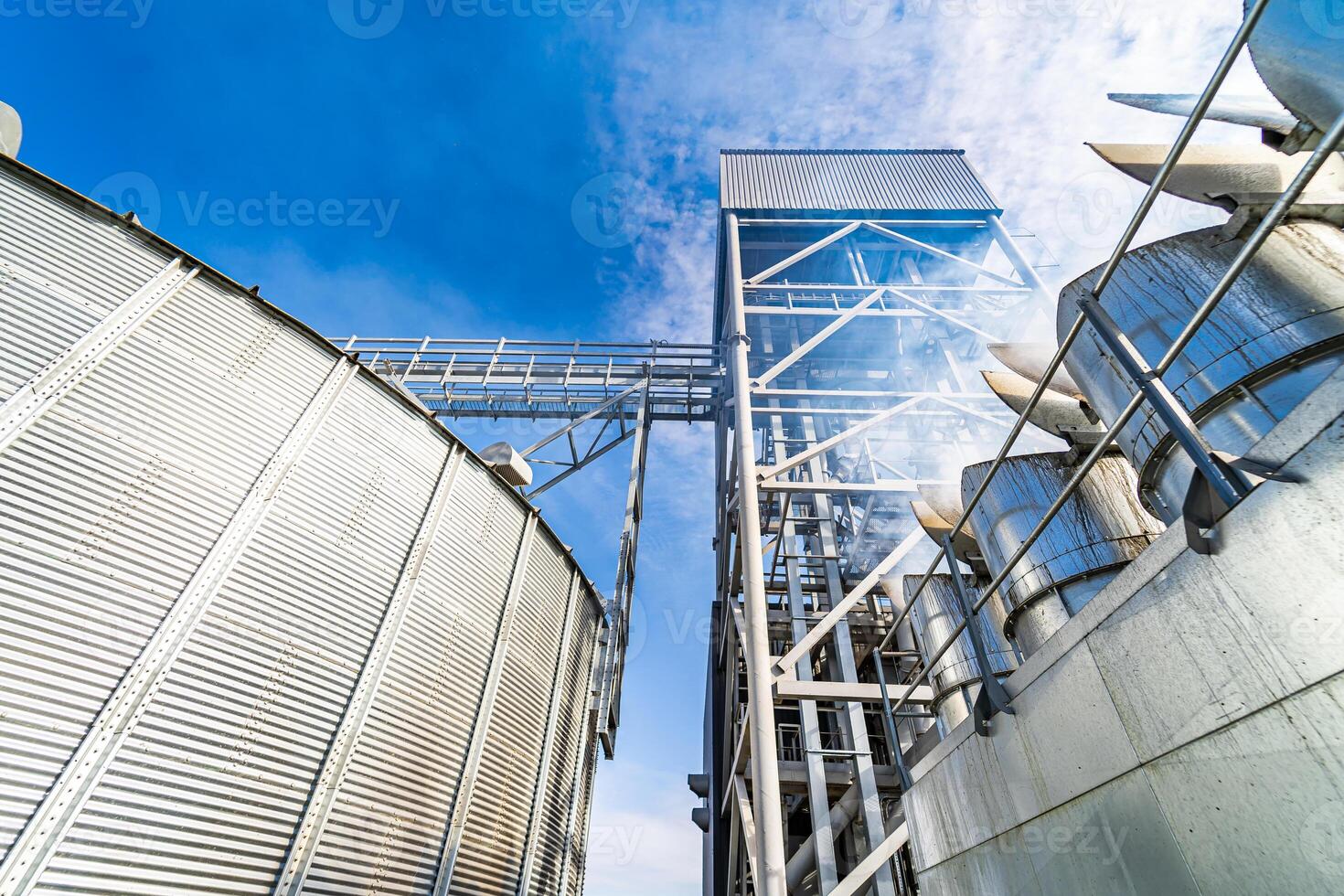 View from below on big tank for grain storage with specially built metal bridge on the top. Cropped photo with part of blue sky.