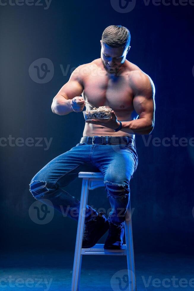 joven muscular hombre participación sano alimento. dieta y sano comiendo concepto. desnudo torso atleta en un silla. foto