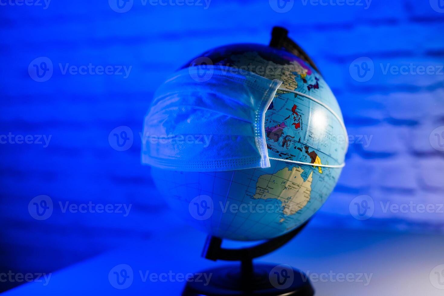 Protective mask on earth globe on blue light background. COVID-19 and coronavirus identification. Pandemic. photo