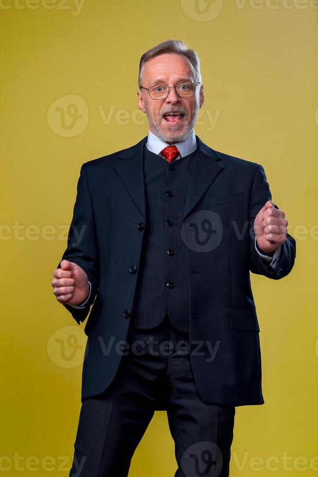 Disparo de contento mayor barbado empresario sonriente mientras bailando y escuchando a música en contra amarillo antecedentes foto