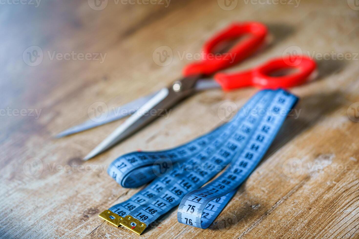 Curved measuring blue tape on wooden table. Scissors with red handle on wooden table. Tailor s concept. photo