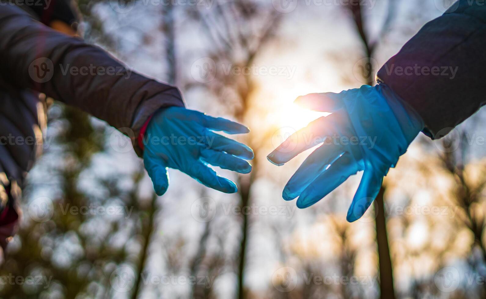 Two hands in rubber medical gloves against sunset . Romantic relationships between people. Protection, isolation and distance during the Covid-19 coronavirus pandemic. photo