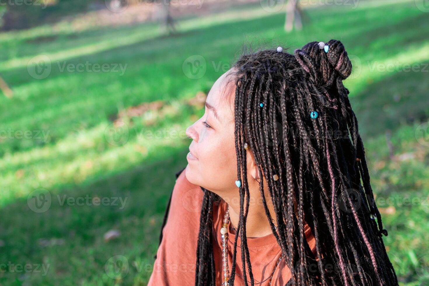 retrato de hermosa europeo mujer con largo africano trenzas mujer es haciendo yoga ejercicio fuera de fuera de en un parque. foto