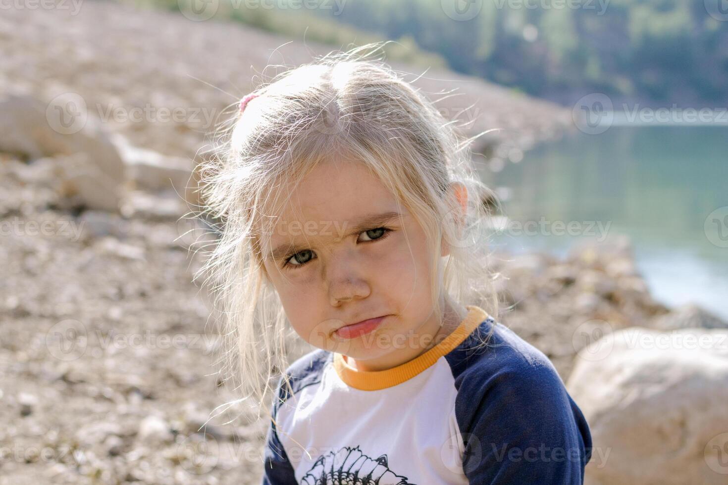 pequeño niña con rubio pelo mirando a el cámara con un triste expresión en su rostro. foto