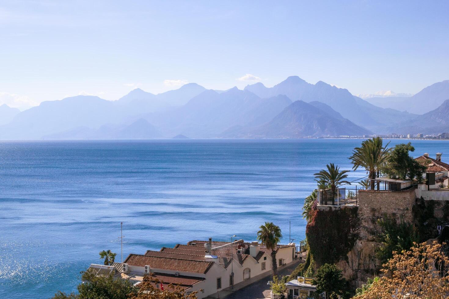 Antalya, Turkey - November 26, 2022. Azure blue sea and distant mountains with white houses on cliff photo