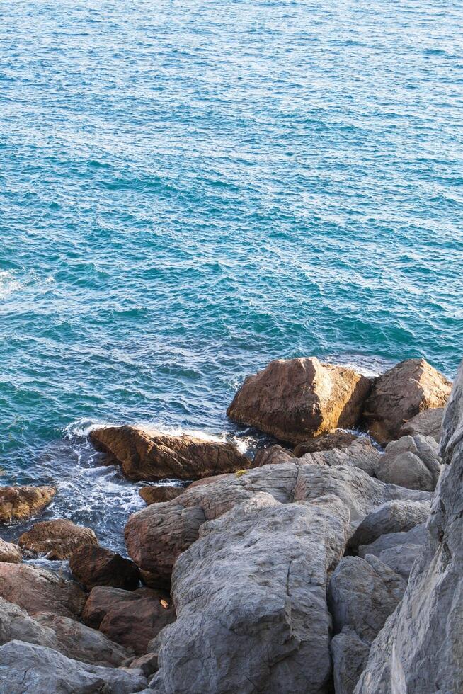 sereno rocoso costa con olas estrellarse en contra cubierto de musgo rocas y claro azul Oceano aguas foto