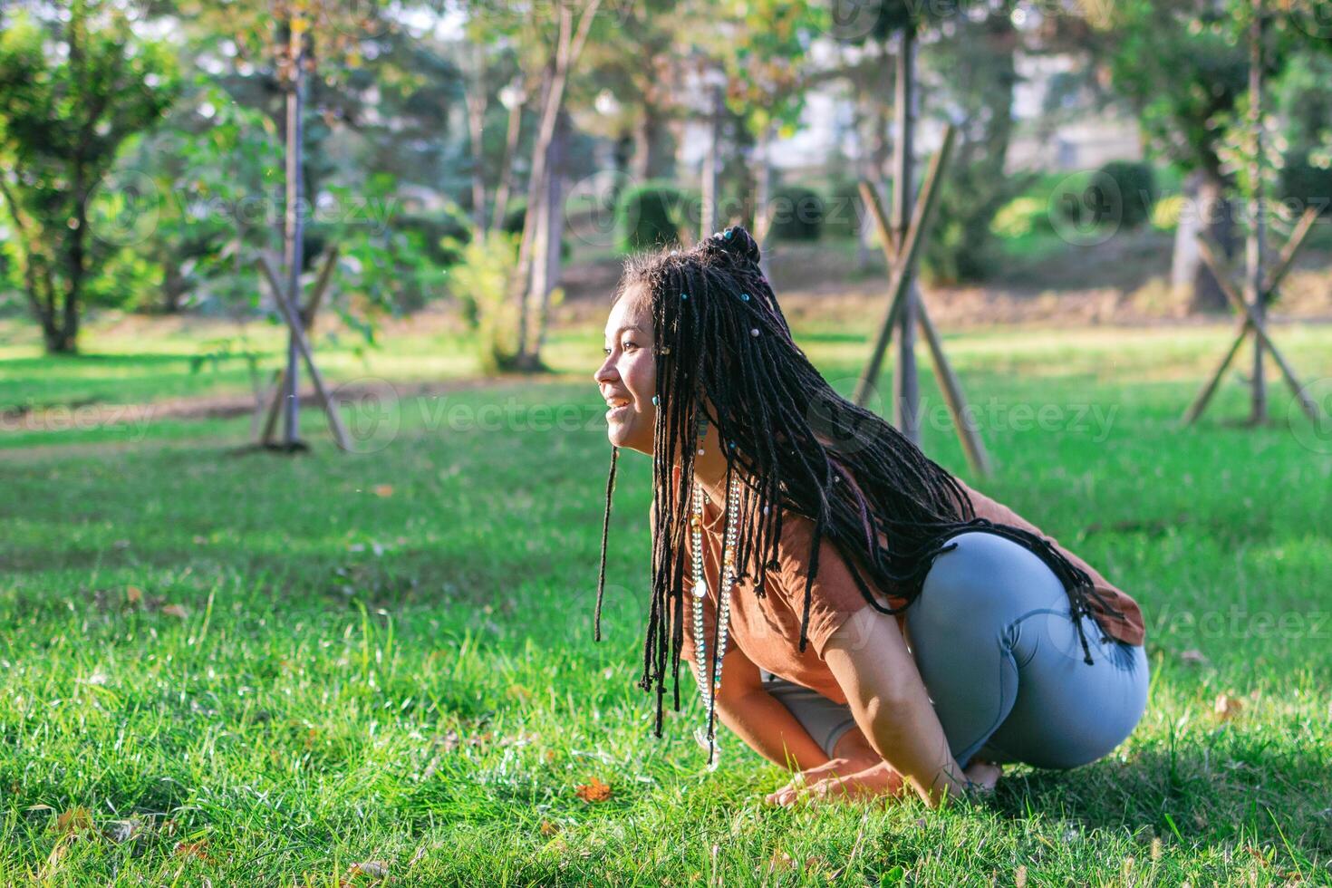 Young woman is sitting on a grass and doing yoga exercise. Healthy lifestyle outdoors. photo