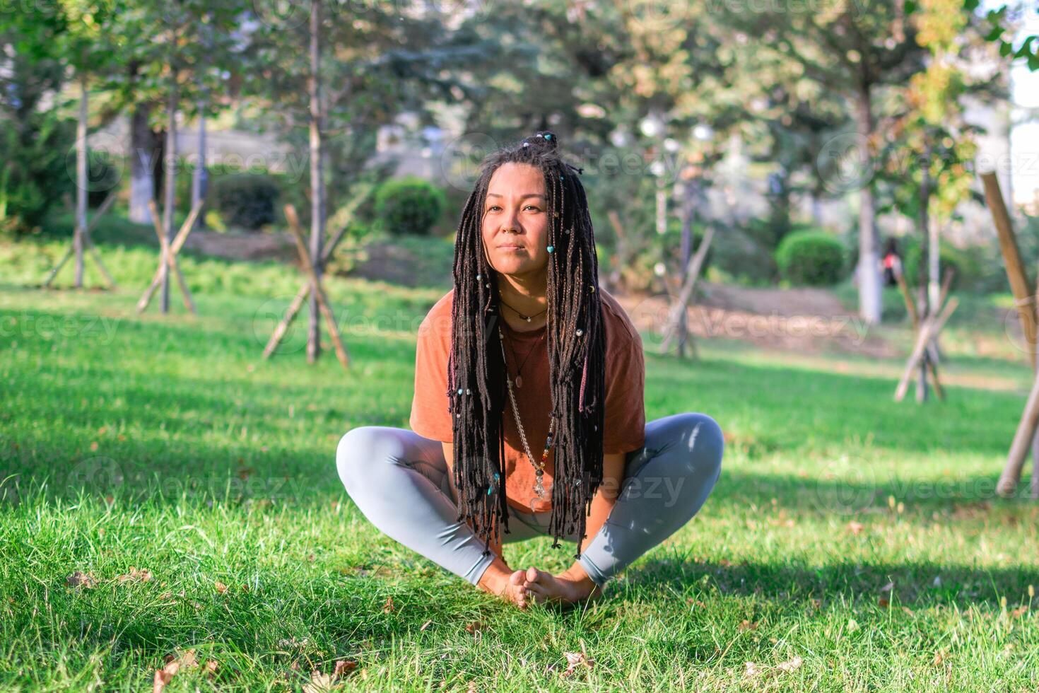 Young European woman is sitting on a grass and doing yoga exercise. Healthy lifestyle outdoors. photo