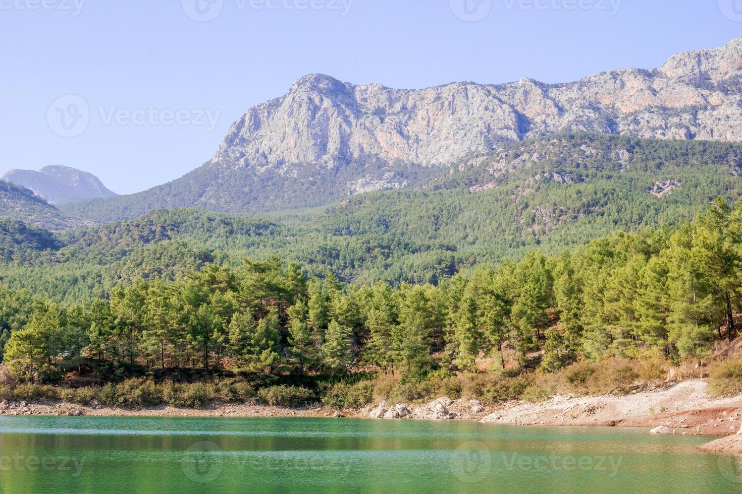 Tranquil lake with snow-capped mountains and pine trees in national park under clear blue sky photo