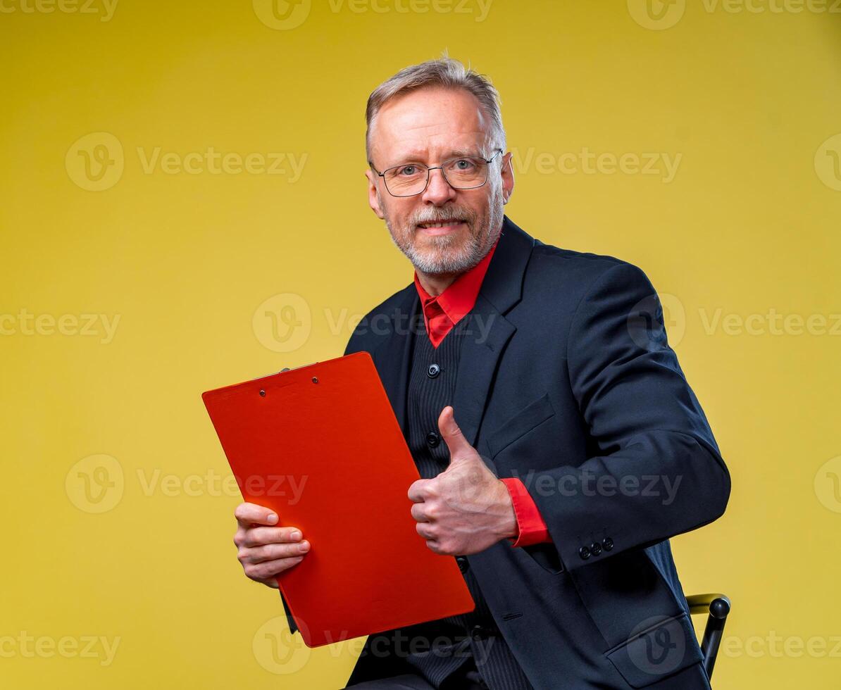 retrato de un sonriente medio Envejecido negocio hombre participación carpeta y demostración pulgar arriba. aislado en amarillo antecedentes. foto