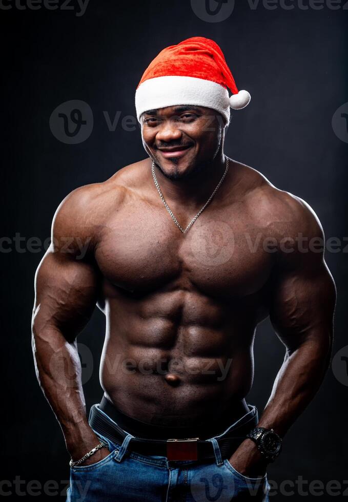 Studio portrait of a good looking happy young black man in Christmas hat posing against black background. Happy New Year concept photo