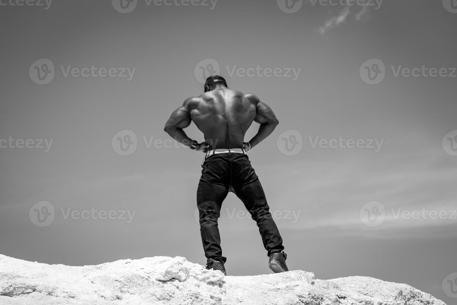 Handsome bodybuilder with naked torso posing outdoor. Athletic man with strong back showing power. photo