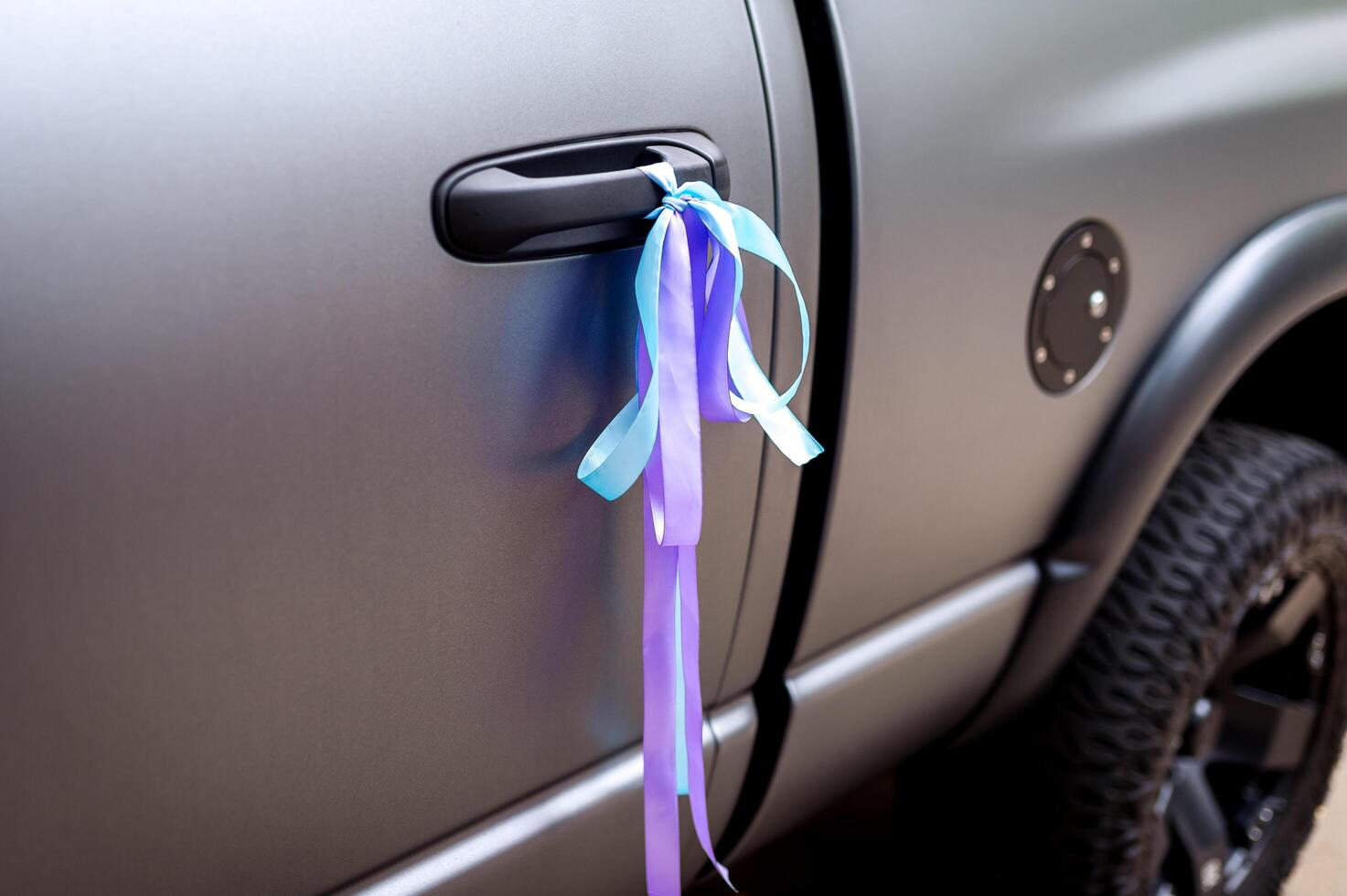 Colorful ribbons on a grey car, decoration for wedding transport. Closeup. photo