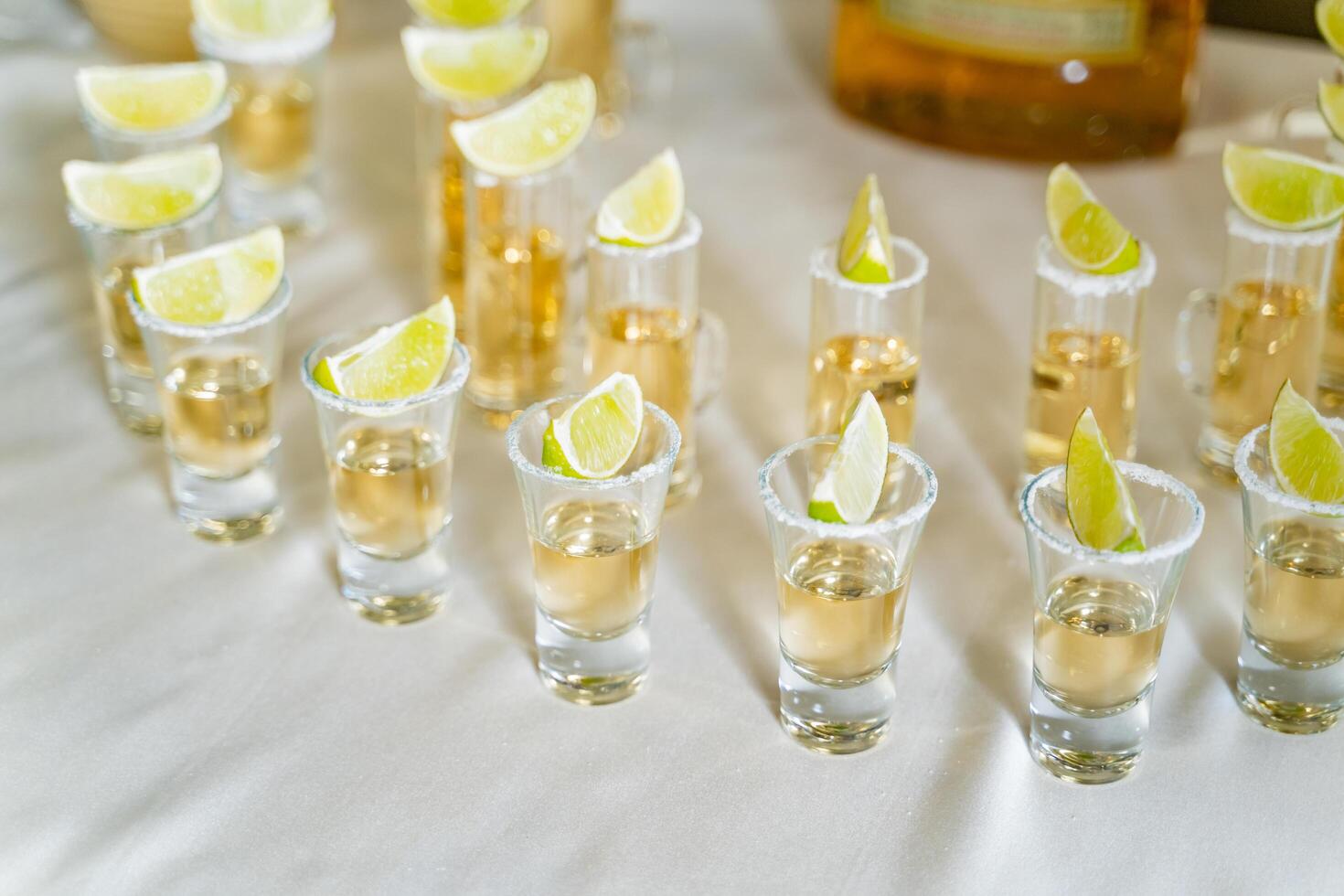 Good service of tequila in small glasses with lime on the white tablecloth. Glasses with vodka, gin, tequila and a slice of lime on them. photo
