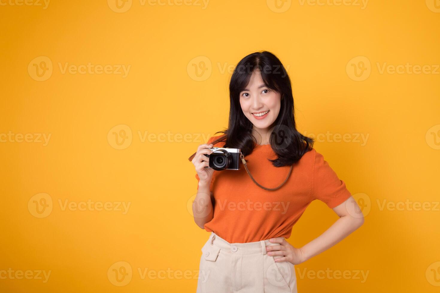 Smiling lady traveler holding a camera isolated on yellow background, illustrating the joy of a holiday journey. photo