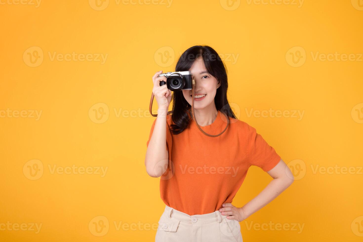 Vibrant woman with camera isolated on yellow background, showing the adventure of exploring new places on her vacation. photo