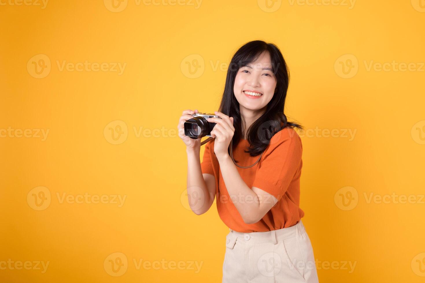 Excited woman traveler capturing her holiday memories with a camera isolated on yellow background. Adventure concept. photo