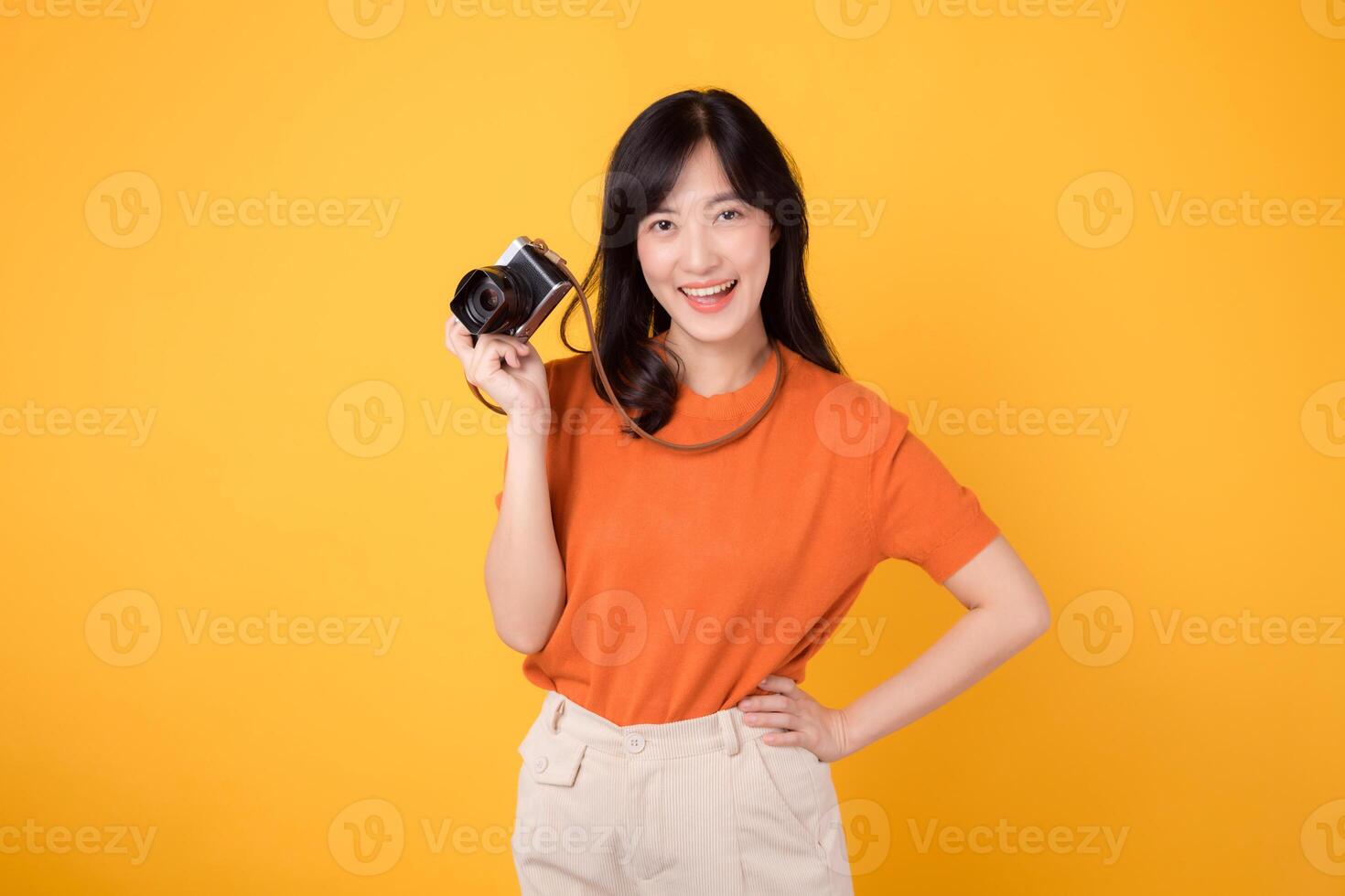 Young asian woman 30s with camera, ready for a fun adventure tour. Positive holiday vibes on a yellow background. photo