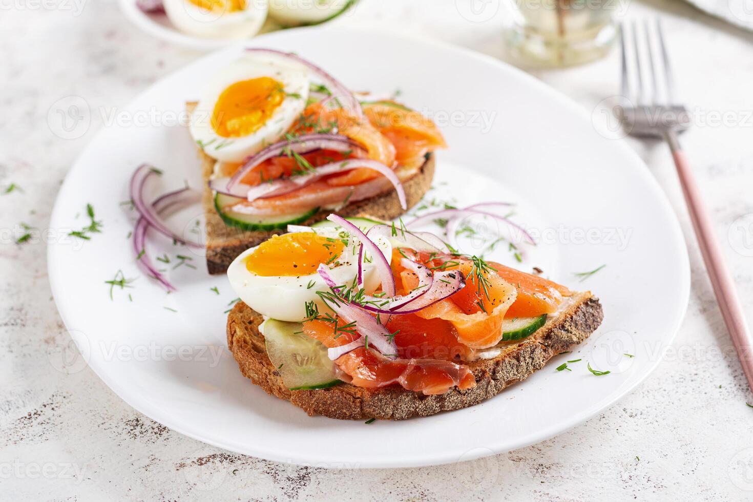 Delicious toast with salmon, boiled egg, cucumber and cream cheese on a white plate. Healthy eating, breakfast. Keto diet food. Tasty food. photo