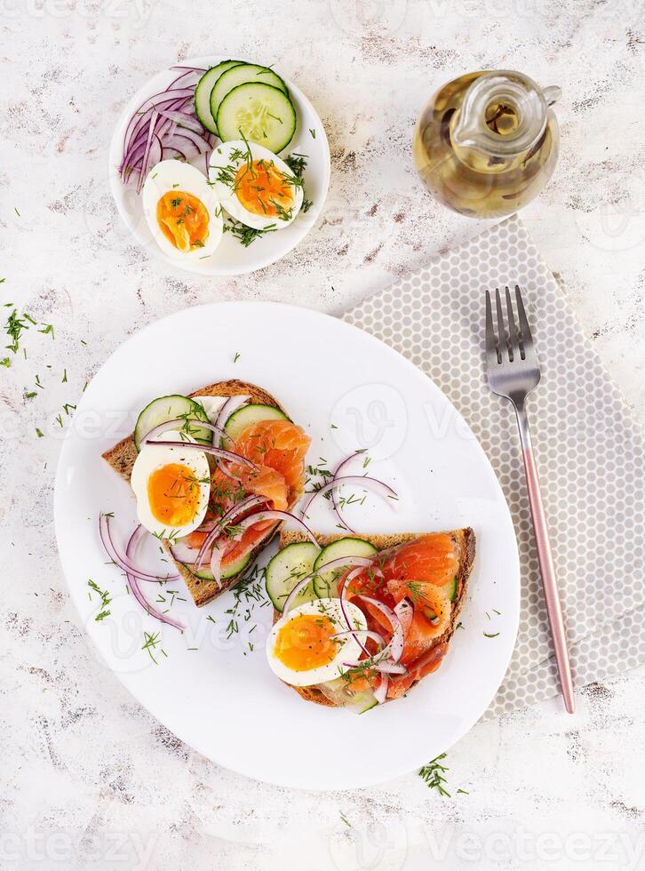 Delicious toast with salmon, boiled egg, cucumber and cream cheese on a white plate. Healthy eating, breakfast. Keto diet food. Tasty food. Top view photo