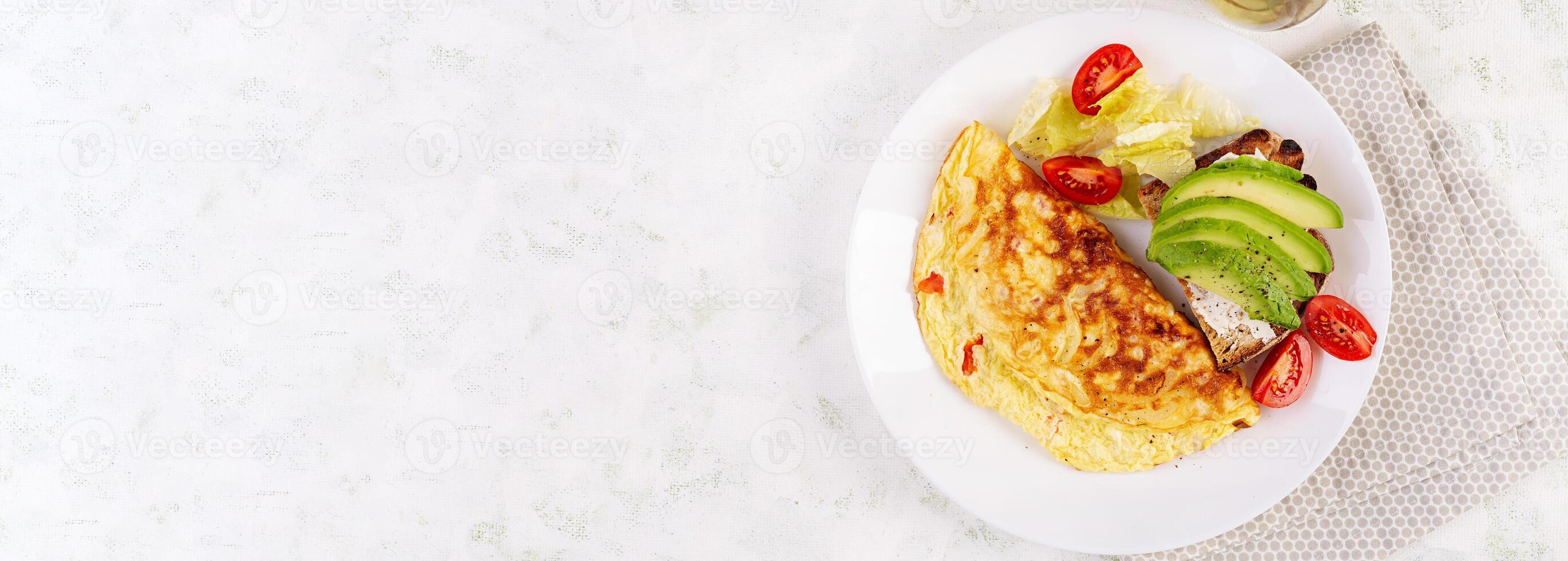 Omelette with tomatoes and toast with avocado on white plate.  Frittata - italian omelet. Top view, banner photo