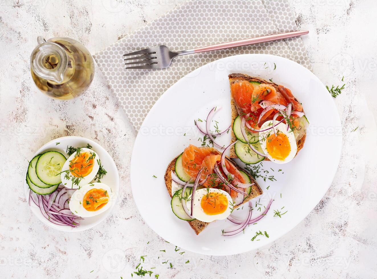 Delicious toast with salmon, boiled egg, cucumber and cream cheese on a white plate. Healthy eating, breakfast. Keto diet food. Tasty food. Top view photo