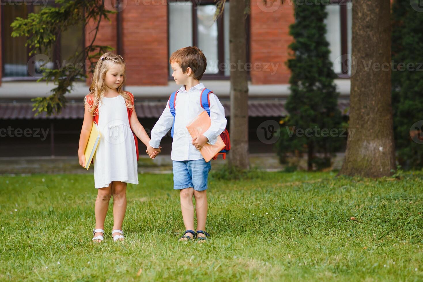 Happy children - boy and girl with books and backpacks on the first school day. Excited to be back to school after vacation. Full length outdoor portrait. photo